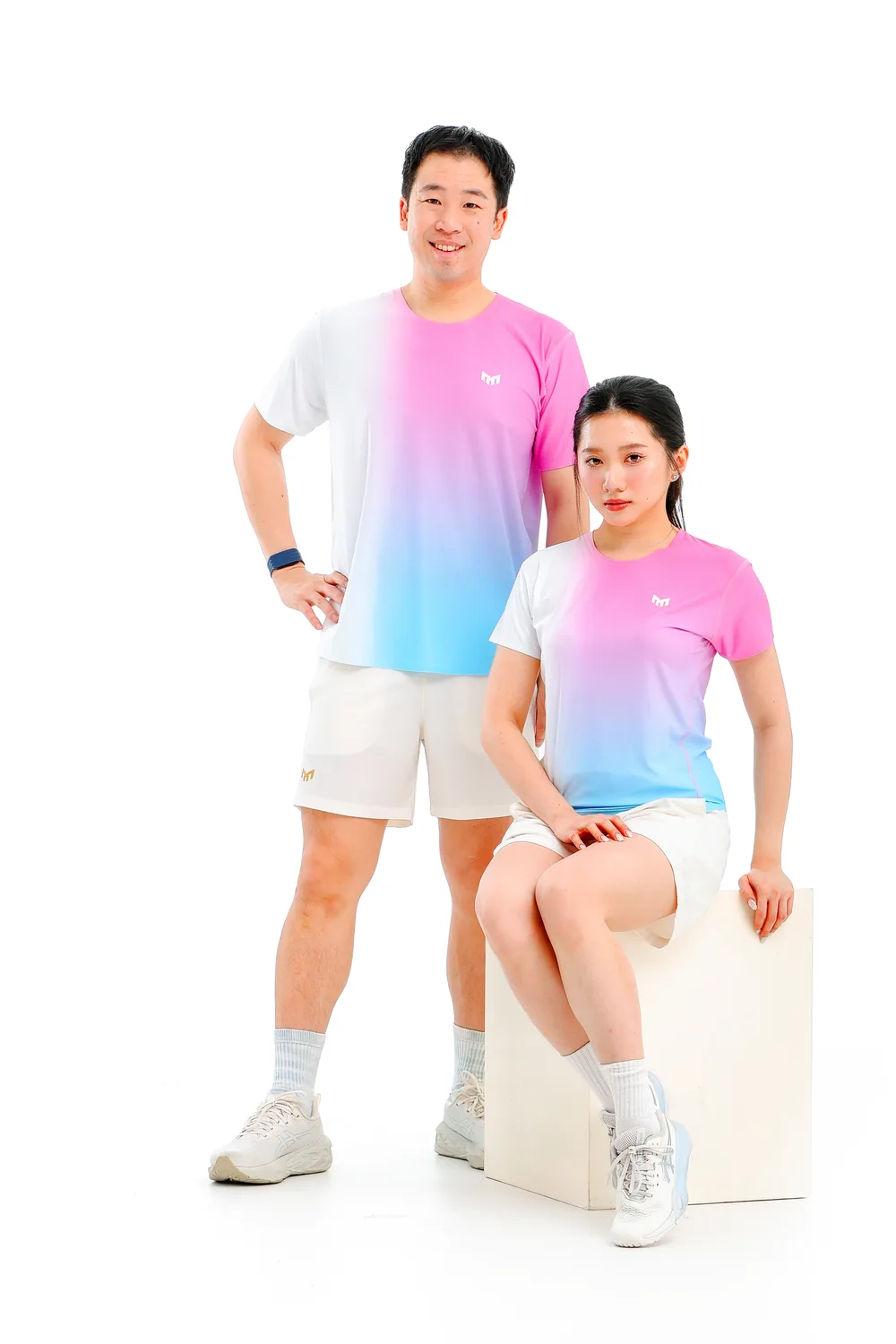 A man in a Cotton Candy T-shirt stands beside a woman in the same T-shirt seated on a block